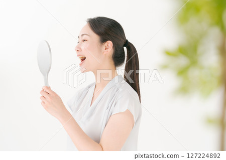 A woman in her twenties looking at her teeth in the mirror A woman in her twenties looking at her teeth in the mirror 127224892