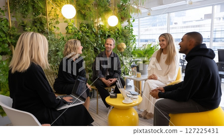 Five professionals engage in a creative discussion in a green office space during daylight hours Five professionals engage in a creative discussion in a green office space during daylight hours 127225431