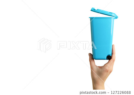 Person's hand lifts a blue trash container high, isolated on white 127226088