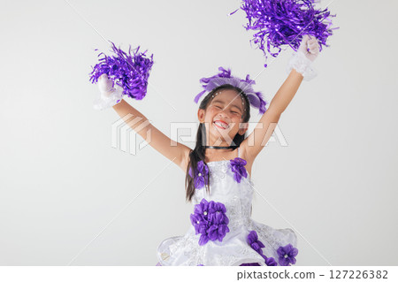 Youthful cheerleader in purple and white outfit holding pom-poms, smiling brightly. Studio image on a clean white backdrop. cheerleader kid Youthful cheerleader in purple and white outfit holding pom-poms, smiling brightly. Studio image on a clean white backdrop. cheerleader kid 127226382