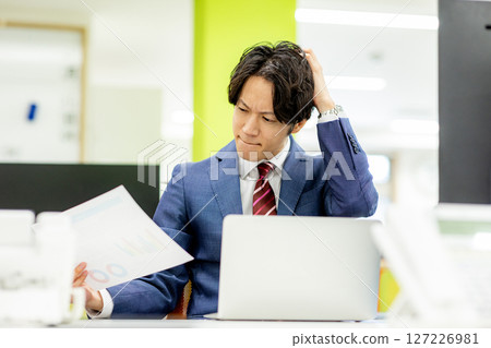 A businessman holding his head while looking at documents 127226981