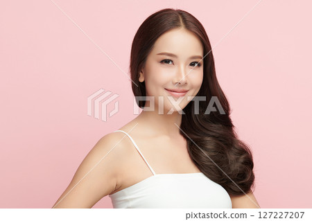 A beautiful young Asian woman with clean, fresh skin against a pink background. Skincare, facial treatment, cosmetology, beauty, and spa. An elegant portrait of an Asian woman. 127227207