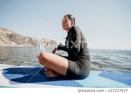 Woman Paddleboard Ocean Smiling, A woman sits on a paddleboard in the ocean, smiling and looking off to the side. 127227637