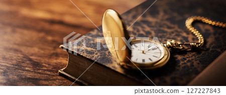 A gold pocket watch on top of an antique book 127227843