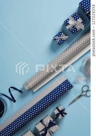 Gift wrapping supplies. Rolls of wrapping paper, scissors, ribbon, ready-wrapped gifts. Blue background, space for your text. Holydays preparation 127228358