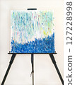 A black easel and a blue abstract painting and canvas depicting rain and the sea 127228998