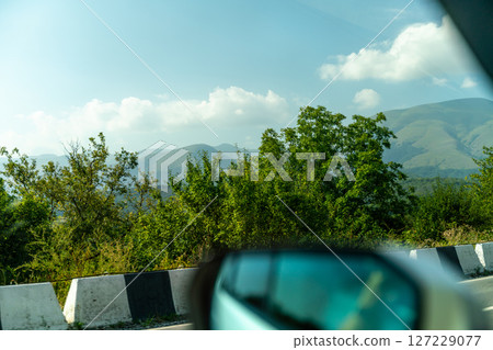 A car is driving down a road with a beautiful mountain range in the background 127229077