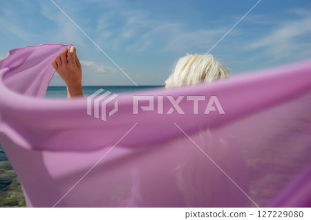 Woman beach shawl: Woman holds shawl to sea, sunbathing during day, enjoying sea breeze 127229080