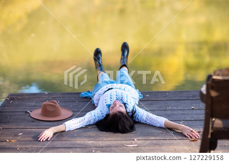 Autumn lake woman. She lies by a pond on a wooden pier in autumn and admires nature. The concept of tourism, weekends outside the city. 127229158