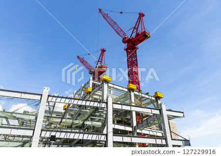 Low-angle view of cranes and steel structures of building construction with a blue sky background in Taiwan. Low-angle view of cranes and steel structures of building construction with a blue sky background in Taiwan. 127229916