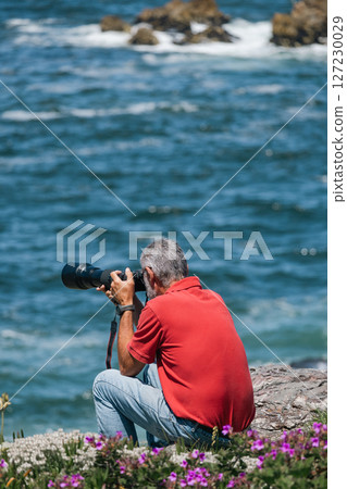 Man in jeans and red t-shirt, photographer with camera taking pictures of ocean 127230029