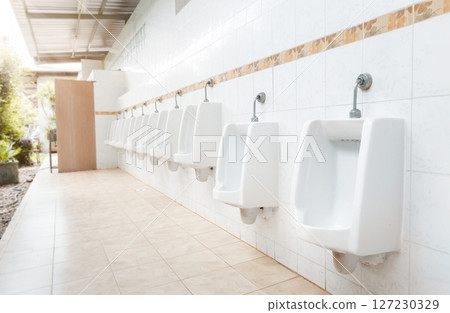 Men's room with white porcelain urinals in line. Modern clean public toilets with tiles . Comfort male toilet urinal concept. 127230329