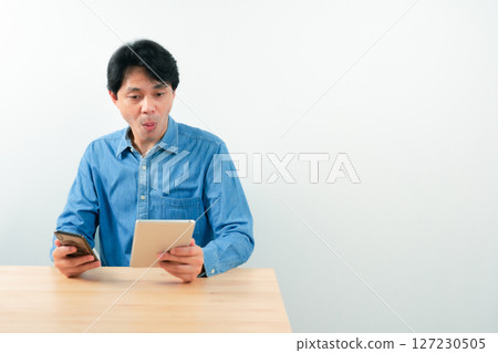asian business man 30s to 40s with blue shirt use tablet for check profit of his startup business with good feeling and white isolated background 127230505
