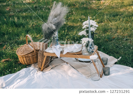 Elegant picnic setup on lush green grass with decorative flowers and unique tableware Elegant picnic setup on lush green grass with decorative flowers and unique tableware 127231291