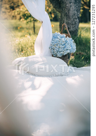 Spacious garden setting with white pillows and blue flowers under a tree 127231295