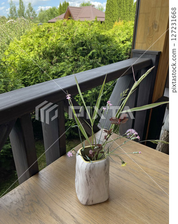 Marble vase with wildflowers on table. Terrace in summer. Design and wooden furniture.  127231668
