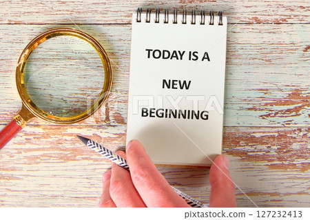 Today is a New Beginning text message written on a notebook. There is a magnifying glass on the wooden surface nearby Today is a New Beginning text message written on a notebook. There is a magnifying glass on the wooden surface nearby 127232413