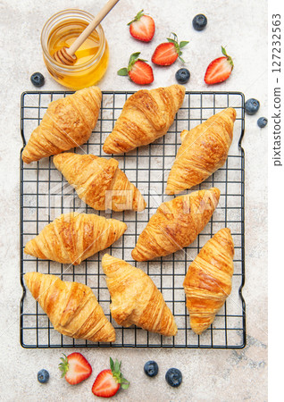 Freshly baked croissants cooling on a wire rack with honey and berries 127232563