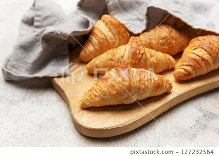 Freshly baked croissants resting on wooden cutting board with linen napkin 127232564