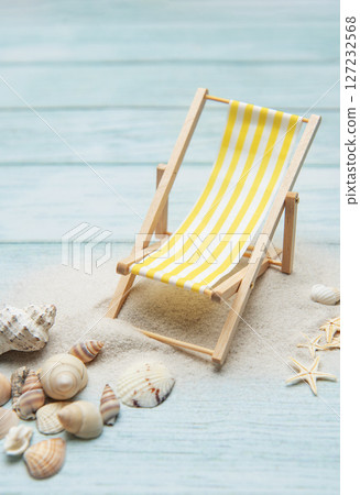 Miniature deck chair on sandy beach with seashells inviting relaxation 127232568