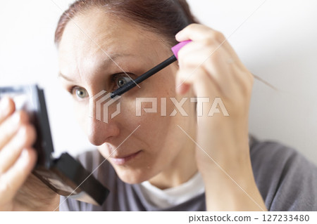 Caucasian woman applying mascara looking in a small mirror Caucasian woman applying mascara looking in a small mirror 127233480