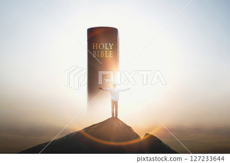 Christian standing with arms raised on top of a high mountain, praising and praying, looking at the holy bible and the cross of Jesus Christ with love in the background Christian standing with arms raised on top of a high mountain, praising and praying, looking at the holy bible and the cross of Jesus Christ with love in the background 127233644