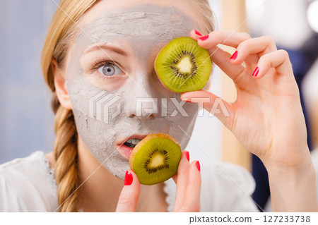 Happy young woman having face mask holding kiwi Happy young woman having face mask holding kiwi 127233738