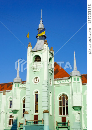 mukachevo, ukraine - jun 16 2012: city council of the old town in morning light. green building with clock tower. popular travel attraction in the city center. empty street in summer. blue sky 127235588