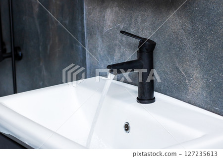 A sleek black faucet is elegantly pouring water into a white sink 127235613