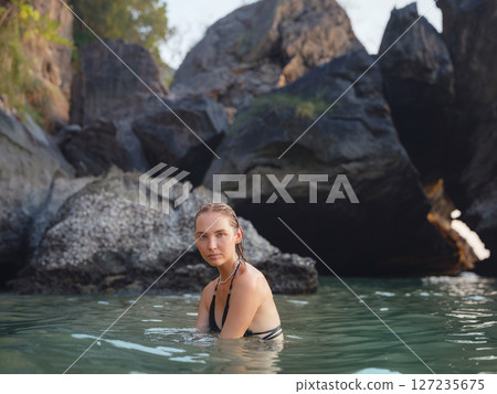 Young woman enjoying serene evening at sea in Krabi, Thailand during sunset. Calm waves, golden light, and peaceful atmosphere highlight tropical beauty and connection with nature. 127235675