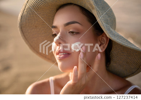 Skincare treatment. Beauty close up portrait of young woman with a healthy skin is applying a facial care product. Cream smear. Sun protection. Girl Uses Sunscreen for Her Skin Skincare treatment. Beauty close up portrait of young woman with a healthy skin is applying a facial care product. Cream smear. Sun protection. Girl Uses Sunscreen for Her Skin 127237414