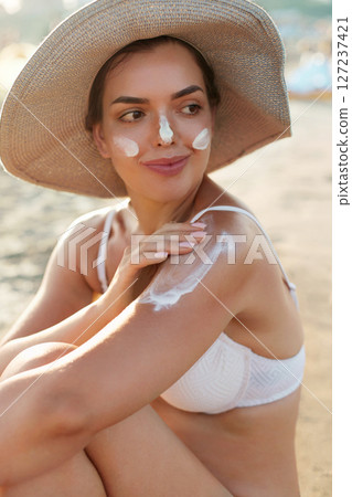 Beautiful Woman in Bikini Applying Sun Cream on Tanned Shoulder. Sun Protection. Skin and Body Care. Girl Using Sunscreen to Skin. Portrait Of Female Holding Suntan Lotion and Moisturizing Sunblock Beautiful Woman in Bikini Applying Sun Cream on Tanned Shoulder. Sun Protection. Skin and Body Care. Girl Using Sunscreen to Skin. Portrait Of Female Holding Suntan Lotion and Moisturizing Sunblock 127237421