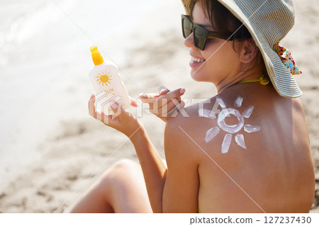 Sun cream on tanned shoulder with sun shape . Sun protection. Beautiful woman in bikini applying  Solar Cream. Skin and body care.Portrait of female holding suntan lotion or moisturizing sunblock 127237430