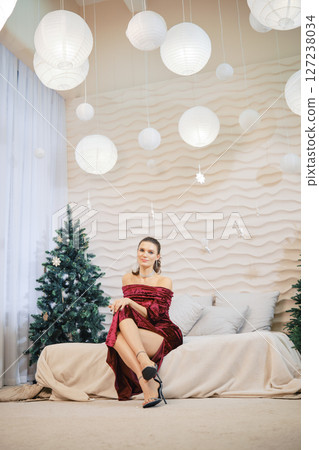Elegant woman in red dress seated on a sofa surrounded by holiday decorations 127238034