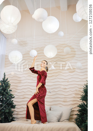 Elegant woman in a red dress poses under decorative lanterns in a cozy interior setting 127238036
