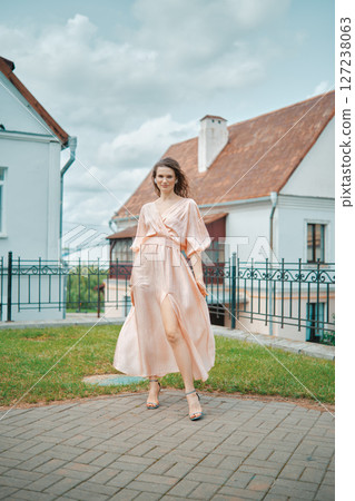 Model walking gracefully in a light dress outside a quaint house on a sunny day 127238063