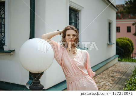 Woman posing by a light fixture near a white building in a sunny outdoor setting 127238071