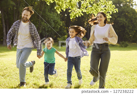 Happy family with two kids running on green grass and having fun in summer park at sunset. Happy family with two kids running on green grass and having fun in summer park at sunset. 127238222