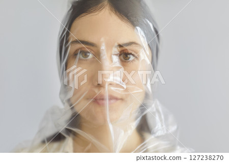 Portrait of beautiful young woman in plastic bag on head looking at camera on gray background. 127238270