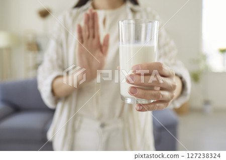 Young woman holding glass of milk and making refusal gesture indicating lactose intolerance. 127238324