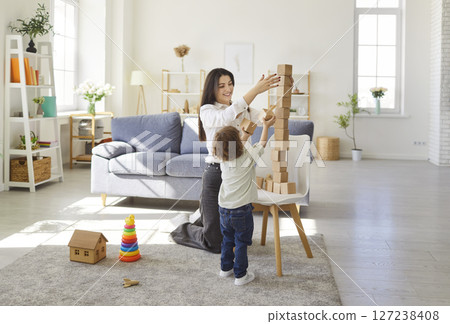 Happy mother helping her little son to build wooden tower of blocks, playing educational game Happy mother helping her little son to build wooden tower of blocks, playing educational game 127238408