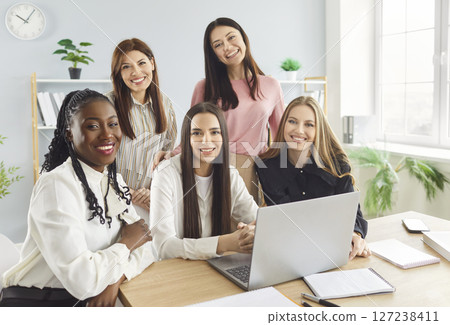 Smiling multicultural businesswomen gathered around desk with laptop working together in office. 127238411