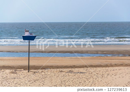 Wooden model of a blue and white boat on pole on a sandy beach, coastal village De Haan, West Flanders, Belgium 127239613