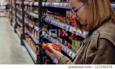 Customer holding a bottle of hot sauce in supermarket, reading label and ingredients, making a choice in grocery store, shopping 127240279