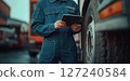 a mechanic in a blue jumpsuit using a tablet while standing next to a truck 127240584