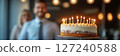Happy birthday cake with candles in the office, blurred background of smiling male coworkers 127240588