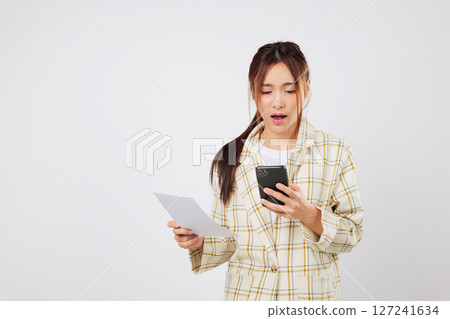Shocked woman holding phone and invoice struggles with financial worries and financial stress while reviewing bill payments. isolated studio white background 127241634