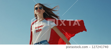 Smiling Woman in Red Cape and Super Mom Shirt on Blue Background Smiling Woman in Red Cape and Super Mom Shirt on Blue Background 127241740