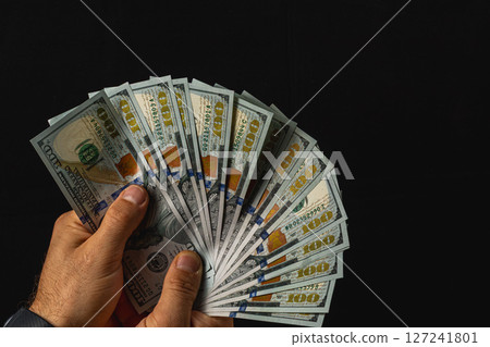 Holding a fan of hundred dollar bills against a dark background Holding a fan of hundred dollar bills against a dark background 127241801