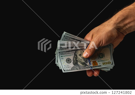Hand clutching stacks of $100 bills on dark backdrop Hand clutching stacks of $100 bills on dark backdrop 127241802